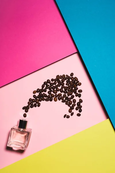 Вид сверху на бутылку духов с кофейными зёрнами на красочной поверхности — стоковое фото