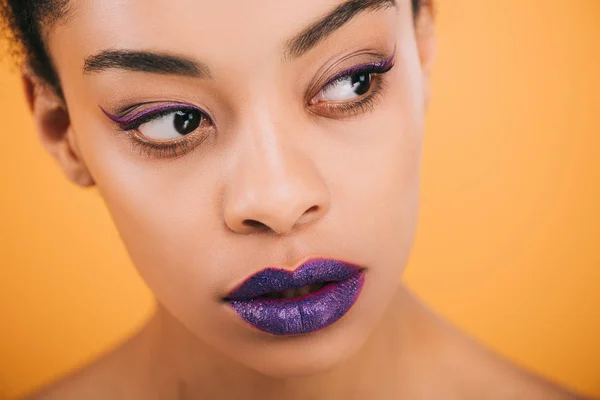 Retrato de cerca de una hermosa joven con labios morados aislados en amarillo - foto de stock