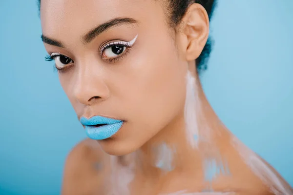 Primer plano retrato de la mujer con maquillaje creativo mirando a la cámara aislada en azul - foto de stock