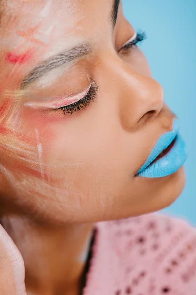 Retrato de cerca de la joven afroamericana con maquillaje creativo aislado en azul - foto de stock