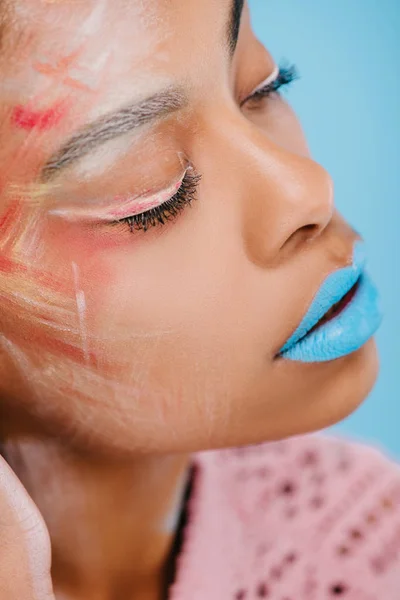 Close-up portrait of young african american woman with creative makeup isolated on blue — Stock Photo