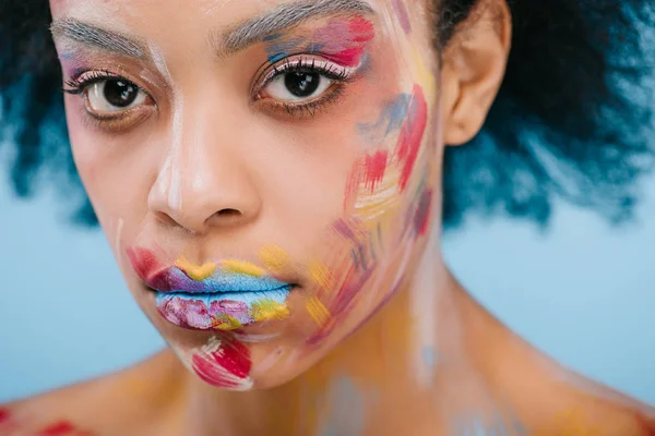 Afro-américaine avec des coups de peinture sur le visage en regardant la caméra isolée sur bleu — Photo de stock