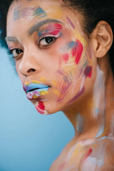 Beautiful young woman with paint strokes on face isolated on blue — Stock Photo