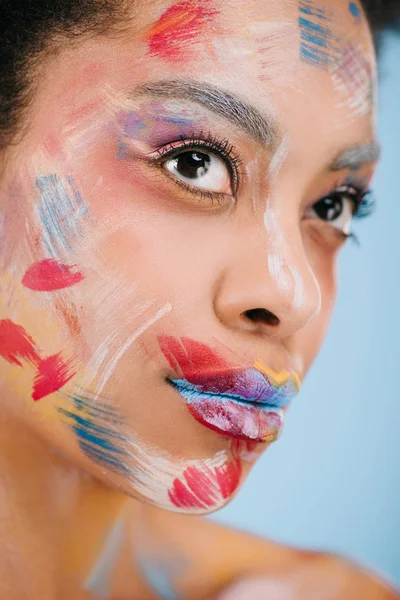 Portrait en gros plan d'une jolie jeune femme avec des traits de peinture sur le visage isolé sur bleu — Photo de stock