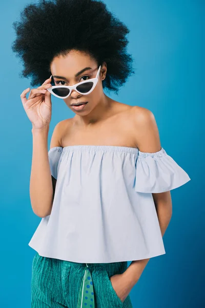 Seductora mujer afroamericana en elegante parte superior fuera del hombro y gafas de sol aisladas en azul — Stock Photo