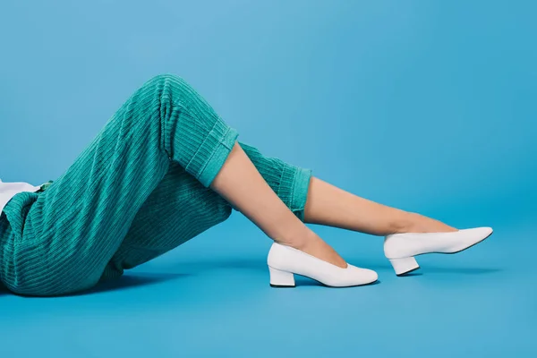 Tiro recortado de la mujer en pantalones elegantes y zapatos que yacen en el suelo en azul - foto de stock
