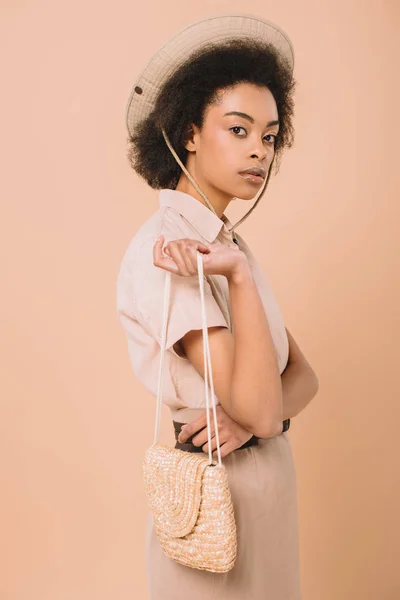 Mujer afroamericana con estilo en sombrero con bolsa aislada en beige - foto de stock