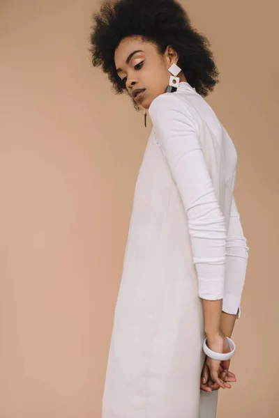 Attractive young woman in white dress with earrings isolated on beige — Stock Photo