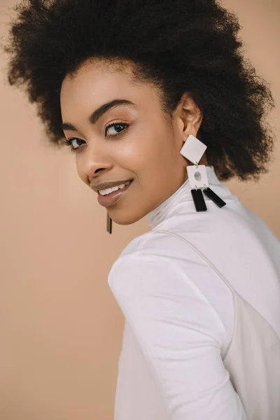 Close-up portrait of smiling young woman in stylish clothes with earrings isolated on beige — Stock Photo