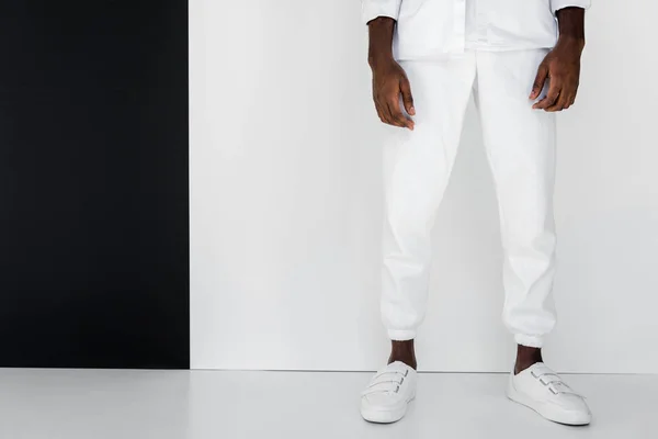 Imagem cortada de homem americano africano elegante em roupas brancas perto de parede preta e branca — Fotografia de Stock
