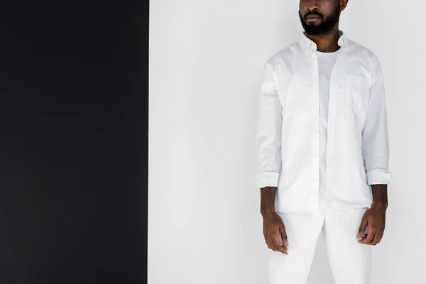Immagine ritagliata di elegante uomo afro-americano in piedi in abiti bianchi vicino alla parete in bianco e nero — Foto stock