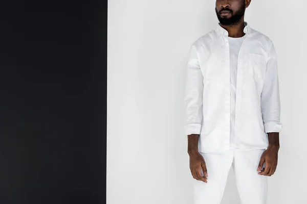 Cropped image of stylish african american man standing in white clothes near black and white wall — Stock Photo