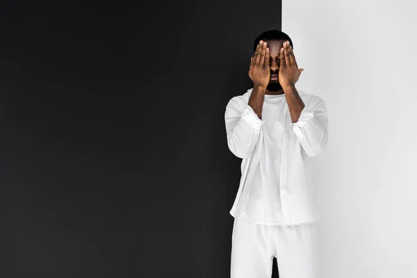 Bel homme élégant afro-américain en vêtements blancs fermant les yeux avec les mains — Photo de stock