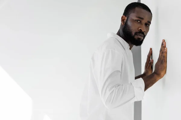 Handsome stylish african american man in white clothes touching wall — Stock Photo