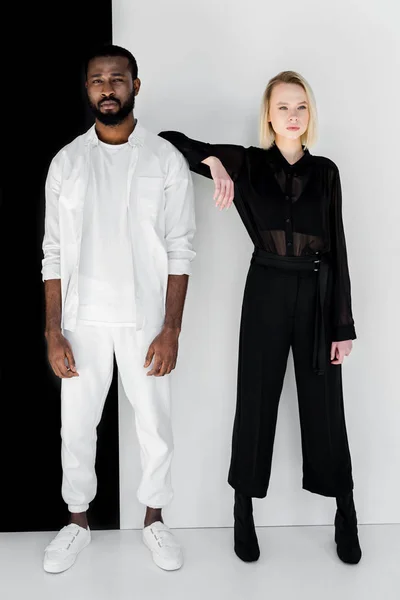 Ragazza bionda alla moda appoggiata al fidanzato afro-americano vicino alla parete in bianco e nero — Foto stock