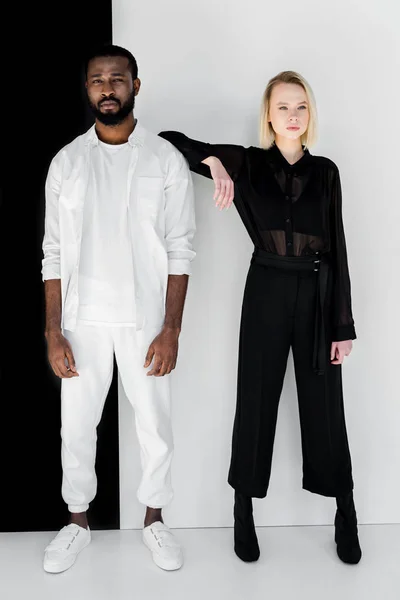 Fashionable blonde girlfriend leaning on african american boyfriend near black and white wall — Stock Photo