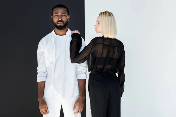 Petite amie blonde touchant petit ami afro-américain près du mur noir et blanc — Photo de stock