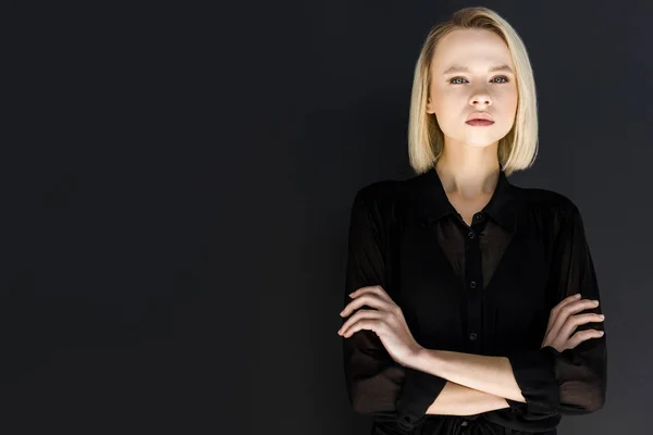 Attraktive, stylische blonde Frau in schwarzer Kleidung mit verschränkten Armen auf schwarzem Hintergrund stehend — Stockfoto