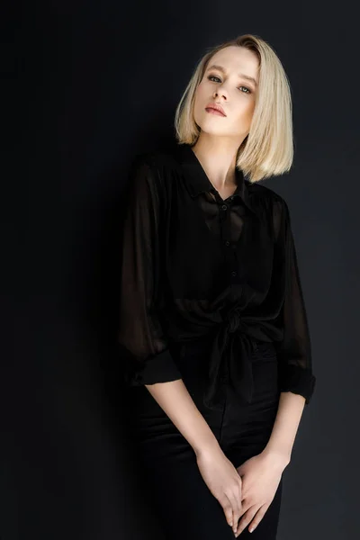 Attractive stylish blonde woman in black clothes looking at camera isolated on black — Stock Photo