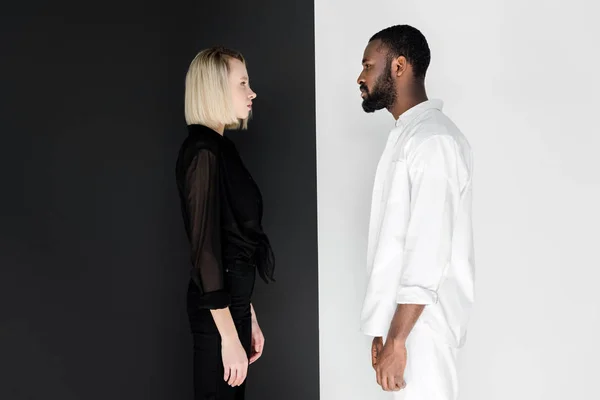 Side view of african american boyfriend and blonde girlfriend looking at each other near black and white wall — Stock Photo