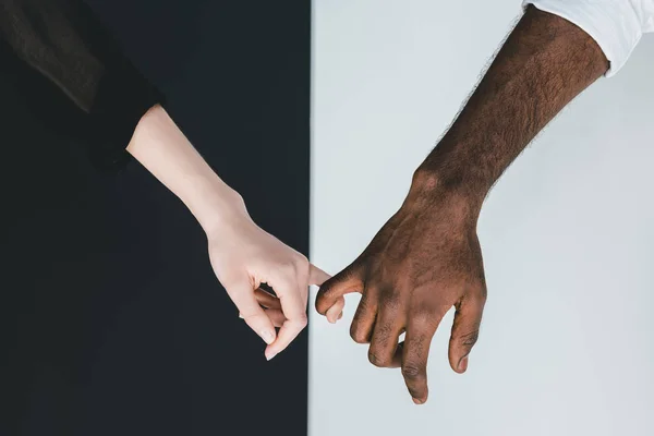 Image recadrée du petit ami afro-américain et sa petite amie tenant les doigts près du mur noir et blanc — Photo de stock