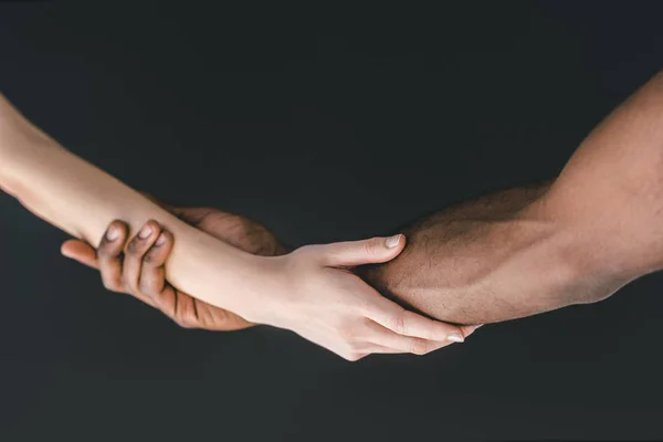 Imagen recortada de pareja multicultural cogida de la mano aislada en negro - foto de stock