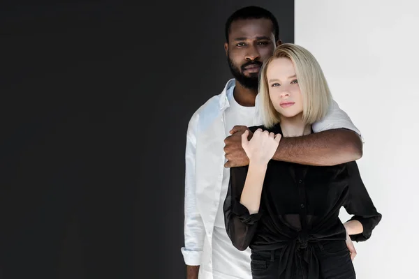 Afro americano namorado abraçando atraente loira namorada perto de preto e branco parede — Fotografia de Stock