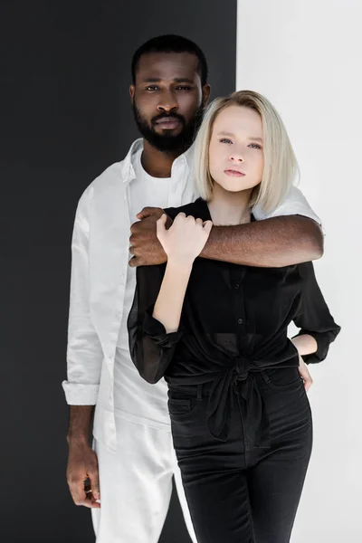 African american boyfriend hugging blonde girlfriend near black and white wall — Stock Photo