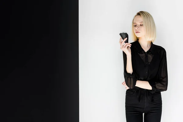 Attractive stylish blonde woman in black clothes looking at ice cream in black cone — Stock Photo