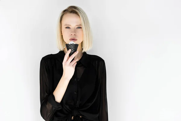 Привлекательная стильная блондинка в черной одежде ест мороженое в черном конусе, изолированном на белом — стоковое фото