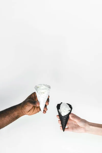 Imagen recortada de pareja multicultural sosteniendo conos de helado aislados en blanco - foto de stock