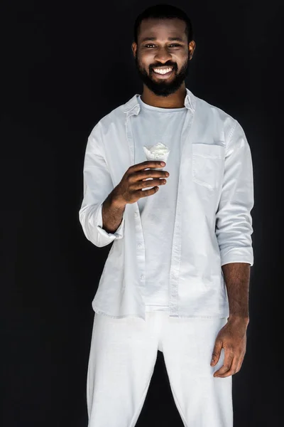 Bonito elegante homem afro-americano em roupas brancas segurando cone de sorvete branco isolado em preto — Fotografia de Stock