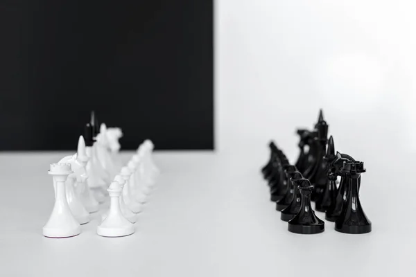 Figuras de ajedrez en filas sobre mesa blanca cerca de la pared en blanco y negro - foto de stock