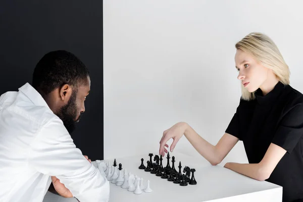Multicultural couple playing chess near black and white wall — Stock Photo