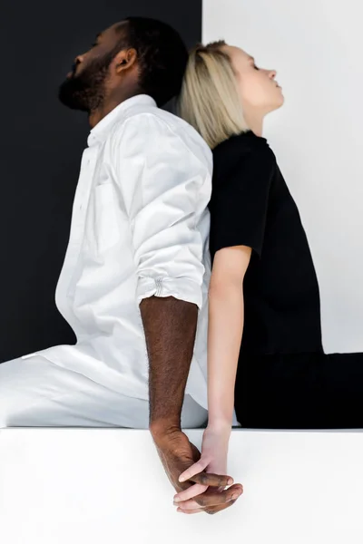 Africano americano novio y rubia novia cogida de la mano en blanco cubo - foto de stock