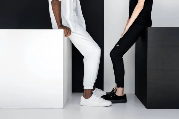 Cropped image of african american boyfriend and girlfriend sitting on black and white cubes — Stock Photo