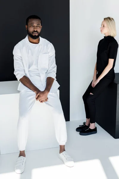 Multicultural couple sitting on black and white cubes — Stock Photo