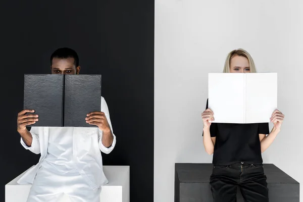 Multicultural couple looking out from black and white books — Stock Photo