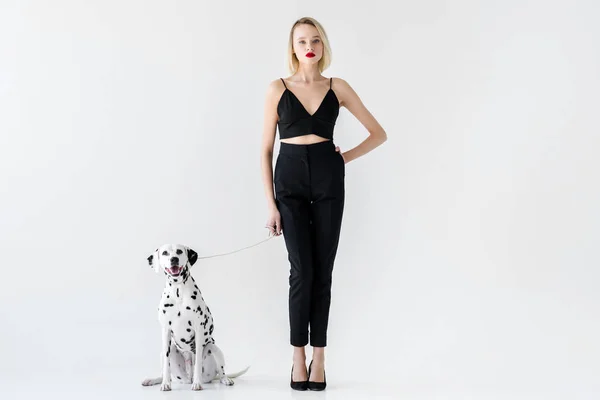 Atractiva mujer rubia con estilo en ropa negra con perro dálmata en blanco - foto de stock
