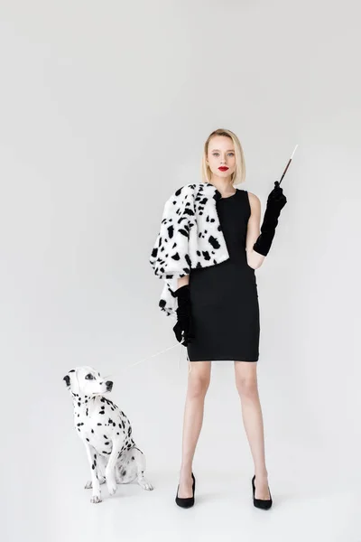 Attractive stylish blonde woman in black dress holding cigarette, dalmatian dog on floor — Stock Photo