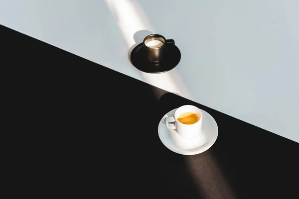 Vista de ángulo alto de tazas blancas y negras de leche y café en la superficie blanca y negra, concepto yin yang - foto de stock