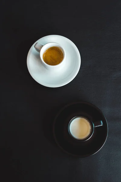 Високий кут зору чорно-білих чашок молока та кави на чорній поверхні — стокове фото
