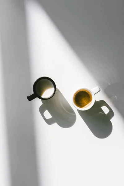 Vue de dessus des tasses noires et blanches de lait et de café sur la surface blanche — Photo de stock