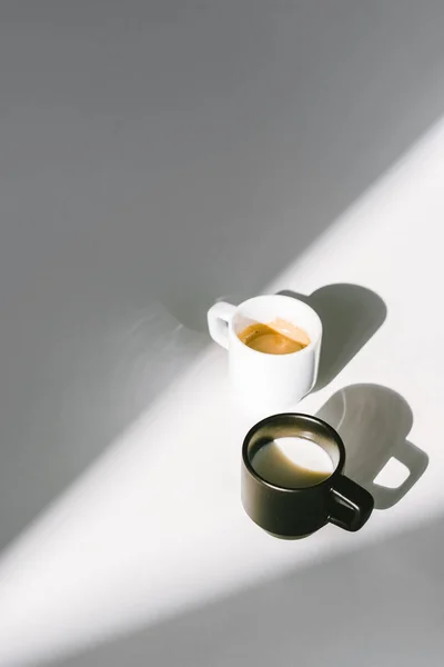 Vista de alto ângulo de copos pretos e brancos de leite e café na superfície branca — Fotografia de Stock