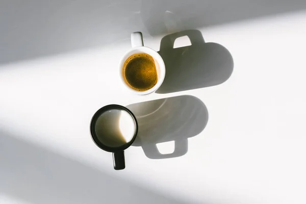 Vue de dessus des tasses noires et blanches de lait et de café sur la table blanche — Photo de stock