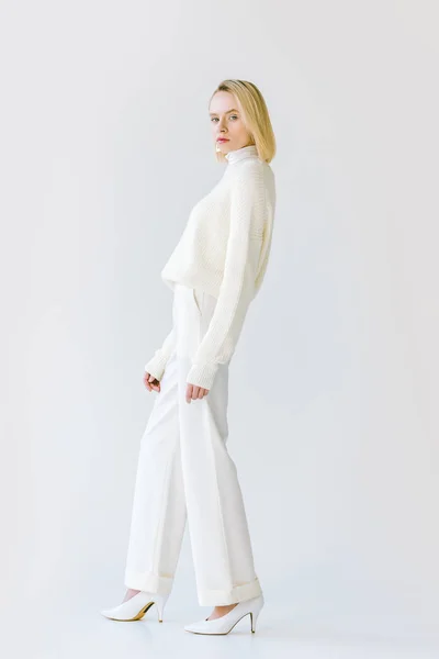 Vista laterale di bella donna bionda elegante in vestiti bianchi guardando la fotocamera su bianco — Foto stock