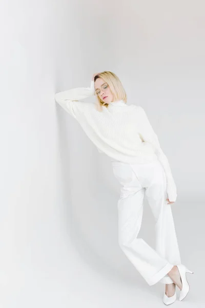 Beautiful stylish blonde girl in white clothes leaning on white wall — Stock Photo