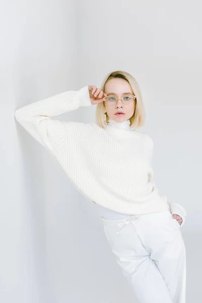 Hermosa mujer rubia con estilo en ropa blanca apoyada en la pared blanca - foto de stock