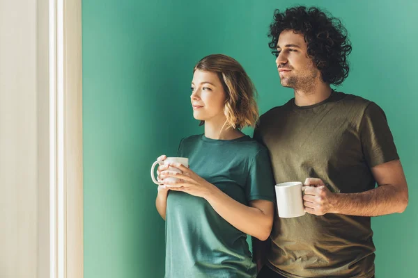 Happy couple in t-shirts holding cups and looking away — Stock Photo