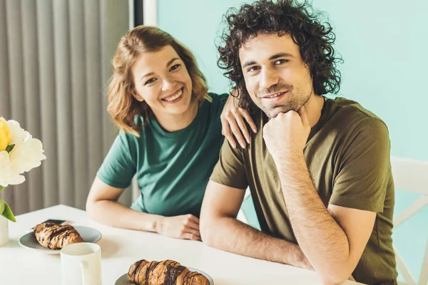 Casal feliz sorrindo para a câmera enquanto tomando café da manhã juntos em casa — Fotografia de Stock